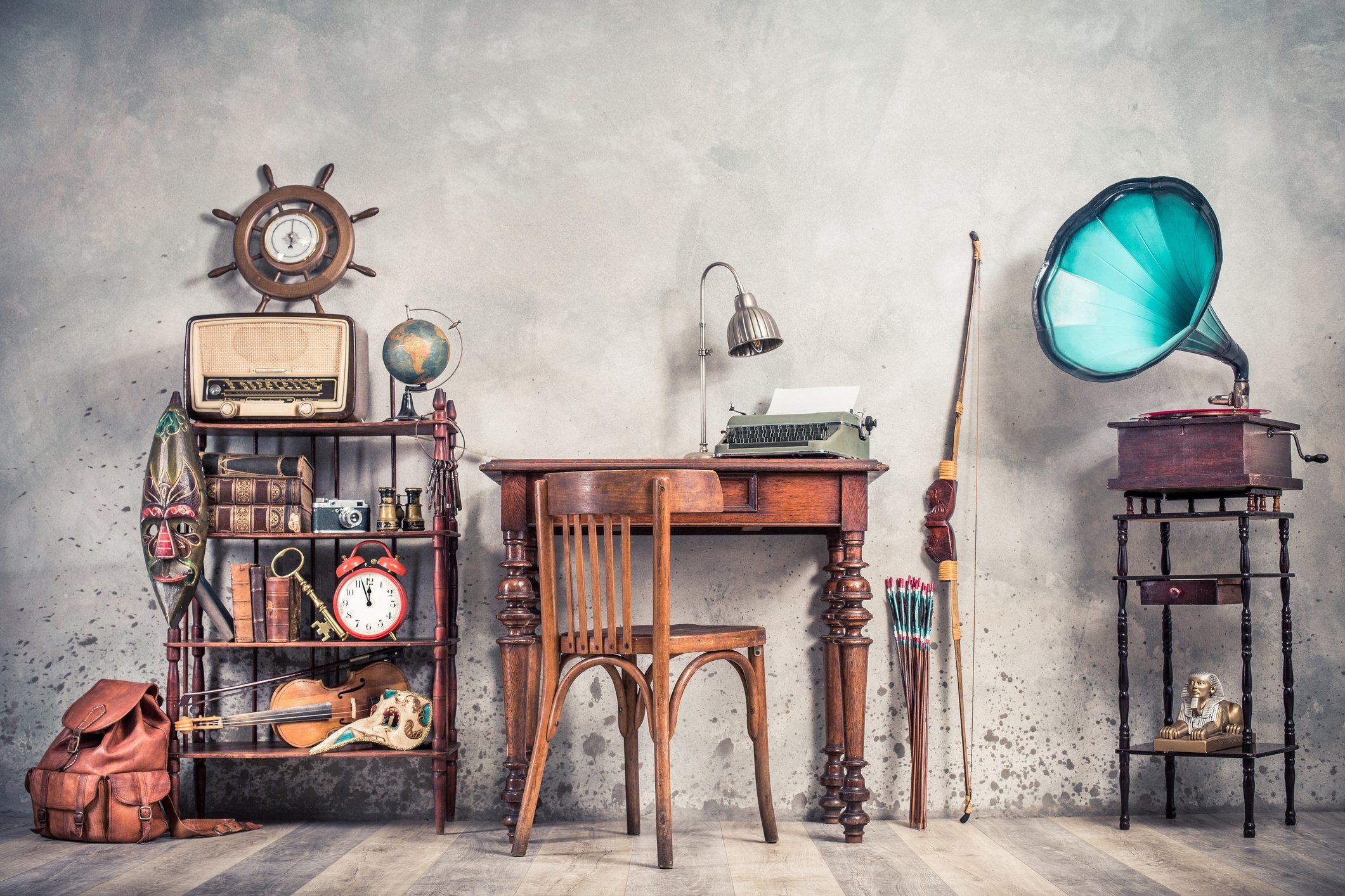 Typewriter on table, vintage gramophone, old books, radio, globe, binoculars, carnival mask, camera, fiddle on shelf, steering wheel, plane, travel backpack, bow. Retro style filtered photo